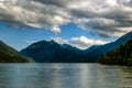 Looking out across lake Crescent with dark deep blue mountains in distance and white fluffy clouds and blue sky