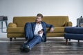 Looking perfect. Handsome young man in full suit using his cell phone while sitting on the floor at home Royalty Free Stock Photo