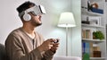 Looking surprised and excited. Young Asian man wearing virtual reality VR goggles while playing games at home Royalty Free Stock Photo