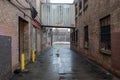 Looking between two vintage industrial brick warehouse buildings with tin metal walkway connection on wet day