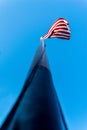 Looking up along a flagpole, toward the American flag, Stars & Stripes, waving in the wind, against a beautiful blue sky on a Royalty Free Stock Photo