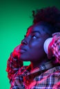 Close-up happy young girl, student listening to music in headphones isolated on dark green studio background in purple