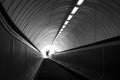 Looking up through a dark inclined escalator tunnel in subway undergraound setting towards bright entrance. Ghostly figure of cycl Royalty Free Stock Photo