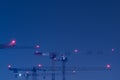 Looking up at group of tall and high tower cranes with red position lights at large construction site for housebuilding at night