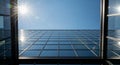 Looking up at a modern glass building facade reflecting the bright sun and clear blue sky Royalty Free Stock Photo