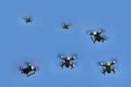 Looking up at multiple small red and black drones flying against a blue sky background