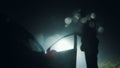 Looking up at a mysterious figure, standing next to a car with the door open, underneath a street light at night. With a blurred, Royalty Free Stock Photo