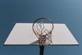 Looking up at old basketball hoop with torn net and white backboard alone against blue sky. Royalty Free Stock Photo