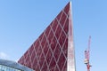 Looking up at shiny red modern and contemporary office building against a blue sky with small clouds and a crane