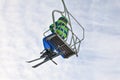 Looking up the skier in green and blue jacket, sitting on simple chairlift, sky with small clouds in background