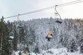 Looking up on skiers sitting on simple chairlift, snow covered trees and overcast sky in background Royalty Free Stock Photo