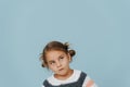 Looking up tight-lipped little girl in striped sweater, hair in buns over blue Royalty Free Stock Photo