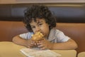 Small curly hair multiracial boy sitting in a coffee shop booth eating a muffin Royalty Free Stock Photo