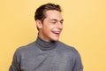 Studio shot of young handsome smiling man, student wearing warm gray polo-neck isolated on yellow studio background. Royalty Free Stock Photo