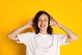 Front view of smiling young beautiful girl in headphones listening to music, audio books isolated on yellow background Royalty Free Stock Photo