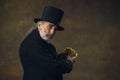 Handsome elderly gray-haired man, gentleman, aristocrat or actor eating fast food isolated on dark vintage background Royalty Free Stock Photo