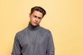 Studio shot of young handsome displeased man, student wearing warm gray polo-neck isolated on yellow studio background. Royalty Free Stock Photo