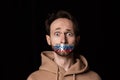 Close-up portrait of young emotive man with three colors duct tape over his mouth isolated on dark background Royalty Free Stock Photo