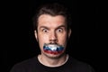 Conceptual portrait of young man with three colors duct tape over his mouth isolated on dark background. Censorship Royalty Free Stock Photo