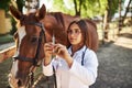 Looks at syringe. Female vet examining horse outdoors at the farm at daytime Royalty Free Stock Photo