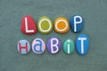 Loop Habit, creative text composed with multi colored stone letters over green sand