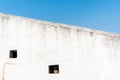 Loopholes and arrowslits on the white wall of a fort