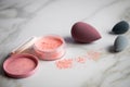 Loose rouge make-up powder with blender sponge on marble beauty table