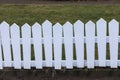 Lopsided white painted wood fence, grass in the back