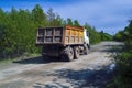 Lorry dump truck rides on a dirt road against the background of the forest and blue summer sky