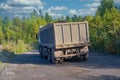 Lorry dump truck rides on a dirt road against the background of the forest and blue summer sky