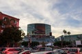 The Los Angeles Convention Center at sunset with cars driving on the street, colorful lights, lush green palm trees, people