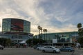 The Los Angeles Convention Center at sunset with cars driving on the street, colorful lights, lush green palm trees, people
