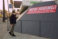 Man wearing mask during Covid pandemic passing Now Hiring banner