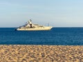 A sleek, white superyacht glides across the calm blue ocean, anchored off a pristine sandy