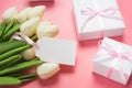 lose up view of white tulips and gift boxes on pink background with blank gift tag.