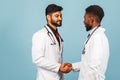 Close-up portrait of a medical worker in a white lab coat with a stethoscope conferring with a young doctor on a blue background