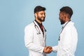 Close-up portrait of a medical worker in a white lab coat with a stethoscope conferring with a young doctor on a blue background