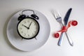 Losing weight. A fork and knife are wrapped in a red measuring tape next to a white plate with a clock white background