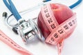 Losing weight with healthy food fruits and vegetables under doctor supervision. Red apple wrapped up by measuring tape and steth Royalty Free Stock Photo