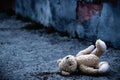 Lost childhood, loneliness, pain and depression. Conceptual image: dirty Teddy bear toy lying down outdoors. Horizontal image.