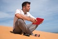 Lost in the desert. Caucasian man sitting on sand with tablet. He is lost and lookking in map where to go Royalty Free Stock Photo