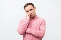 Gloomy man in pink shirt, holding hands on face, frowning and staring with helpless expression Royalty Free Stock Photo