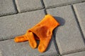 A lost orange cloth glove is lying on the pavement