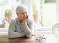 Lost in pleasant memories. A senior woman sitting at her kitchen table lost in thought.