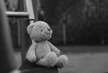 Lost teddy bear sitting on swing at playground in gloomy day, Lonely and sad face brown bear doll sitting alone in the park, lost