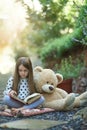 Lost in the wonder of her favourite story. a little girl reading a book with her teddy bear beside her. Royalty Free Stock Photo