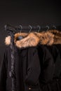 lot of black coats, jacket with fur on hood hanging clothes rack. background.