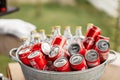 a lot of bottles of coca cola in the steel bowl with ice on wooden table outdoors. fresh beverage ready for summer party