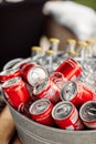 a lot of bottles of coca cola in the steel bowl with ice on wooden table outdoors. fresh beverage ready for summer party