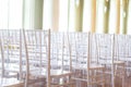 A lot of chairs indoors near the window. Rows white chairs in the hall. Empty room with many modern seats, nobody in big lobby.